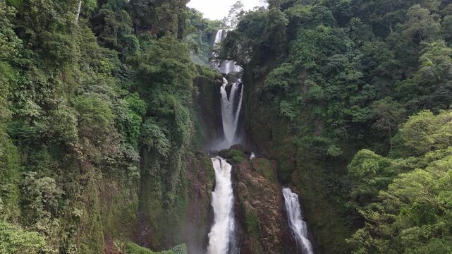 Aerial view of Curug Klenting Kuning waterfall cascading through lush tropical forest and dense green trees in Kecamatan Limbangan, Central Java, Indonesia.