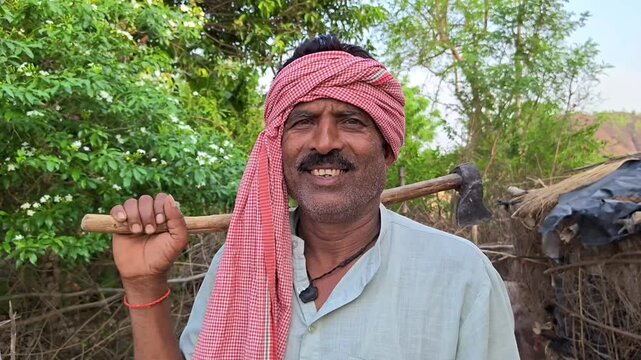 Smiling indian farmer holding an axe on his shoulder