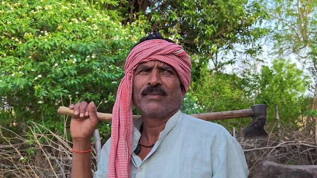Indian farmer standing in field holding axe on his shoulder