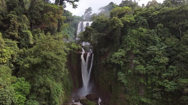 Aerial view of Curug Klenting Kuning waterfall cascading through a dense tropical forest with lush green foliage in Kecamatan Limbangan, Central Java, Indonesia.