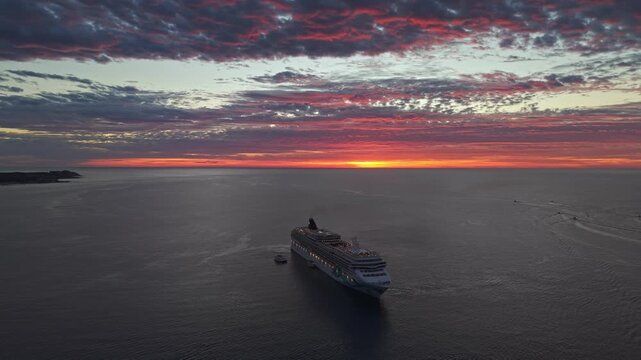 Aerial orbit establishing a massive cruise ship at sunset with voluminous clouds in the background, off the coast of Los Cabos, Mexico