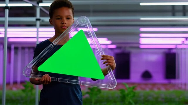Young boy holding a futuristic green screen display in a modern vertical farm