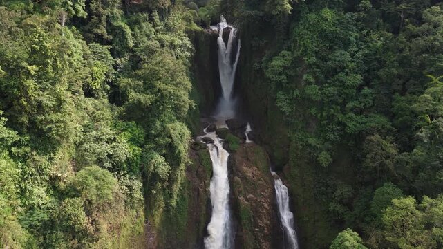 Aerial view of Curug Klenting Kuning waterfall cascading down rocky cliffs surrounded by lush tropical jungle in Kecamatan Limbangan, Central Java, Indonesia.
