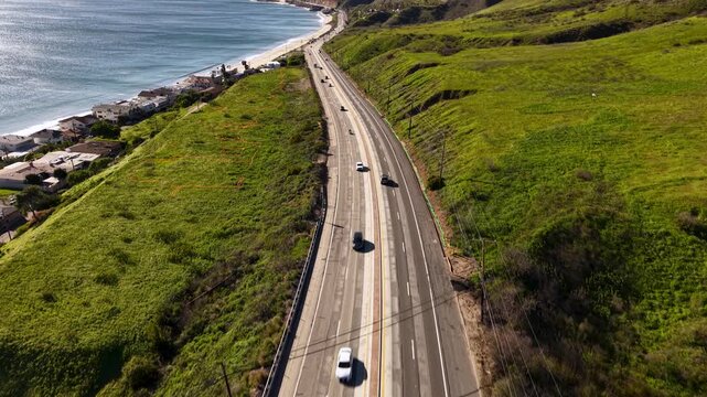 Malibu Beach PCH Pacific Coast Highway curving along the Malibu coastline, road and beach pattern visible from directly above on a clear sunny California day. Green grassy hillside.