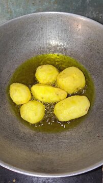 Deep frying whole peeled potatoes in hot bubbling oil closeup