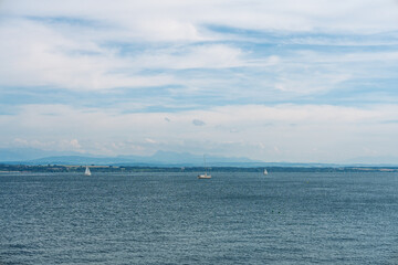Obraz premium Sailboats glide across Lake Constance in Germany beneath a cloudy sky, framed by distant mountains and calm waters that convey a peaceful leisure scene and open natural vista.