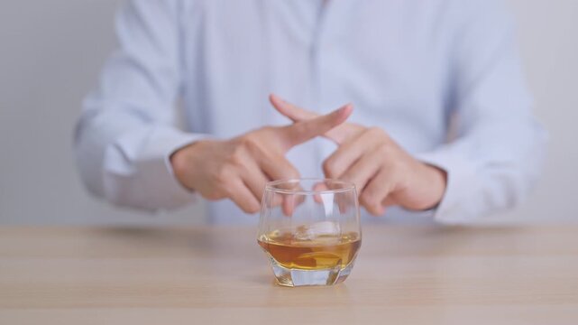 Man making stop hand gesture to refuse a glass of Cognac, Healthy man say no to alcohol drink, stop alcoholism and addiction concept. Responsible man reject a drink before driving and quit booze
