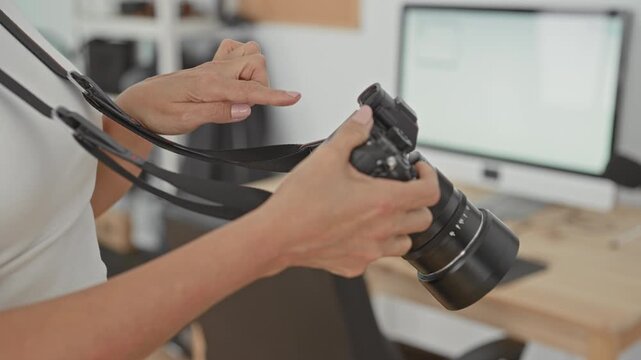 Middle aged hispanic woman photographer points finger to camera controls adjusting lens with hands in studio; concentration craft technique.