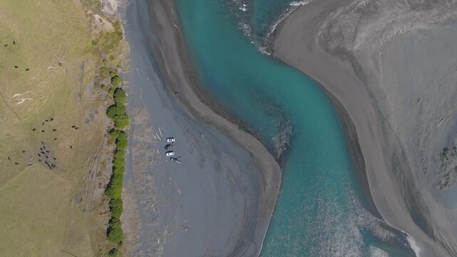 Aerial view of people with vehicles on the braided riverbed of the Marokopa River, in the Waitomo region of New Zealand. The turquoise water flows through the landscape.