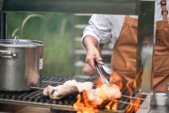 Barbecue grill with chef cooking chicken over open flame in outdoor kitchen