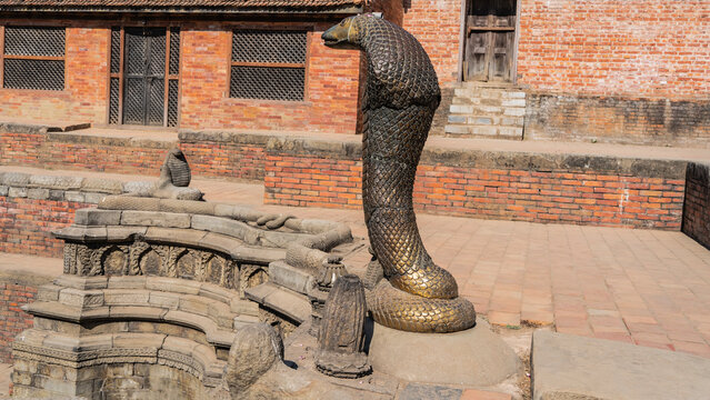 Ancient Newar architecture. Naga Pokhari  water tank. Sculpture of a cobra by the pool. A metal statue of a snake with its head raised. Carved stone perimeters of the reservoir. Nepal. Kathmandu.