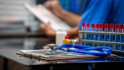 Obraz premium Medical lab desk with clipboard and stethoscope in foreground, test tubes in rack, healthcare worker blurred in background, clinical setting, shallow depth of field.