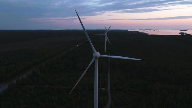 Aerial view toward a wind power generator against a dramatic cloudy dusk sky.