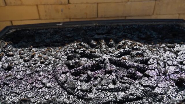 Heavy creosote and tar buildup on cast iron fireplace grate close up. Thick black sticky deposits on wood stove bottom plate