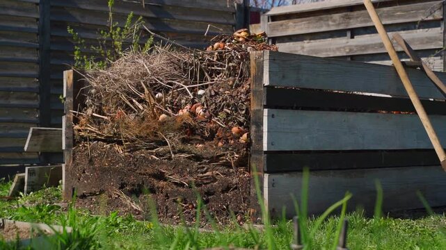 Wooden compost bin filled with layered organic waste in backyard garden on sunny spring day