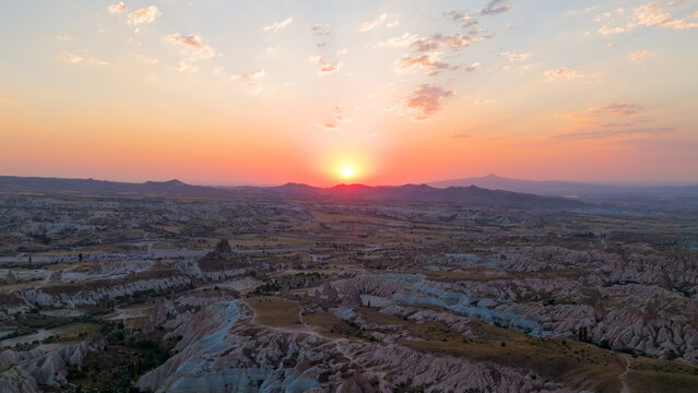 Goreme, Nevsehir, Turkey. Drone view of Red Valley at sunset with distant mountains, plateaus and sunrays illuminating clouds in Cappadocia sky.. Aerial View