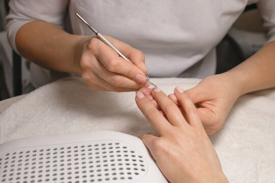 Professional nail technician shaping cuticles during manicure in beauty salon, close-up hands on white towel, soft neutral colors, clean spa care mood