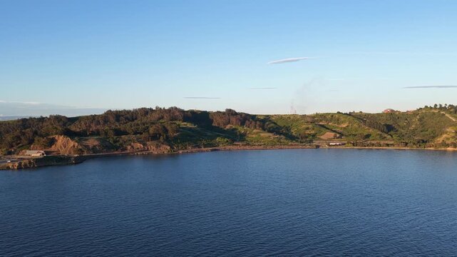 Aerial drone footage flying sideways over the calm water of the San Pablo bay with a view of the Richmond coastline in California during a beautiful sunset, capturing the golden light on the hills