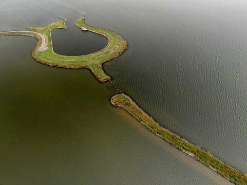 Aerial view of Tulpeiland, a tulip-shaped artificial island with green grass and stone embankments in the calm waters of Wolderwijd lake Wolderwijd, Flevoland, Netherlands.
