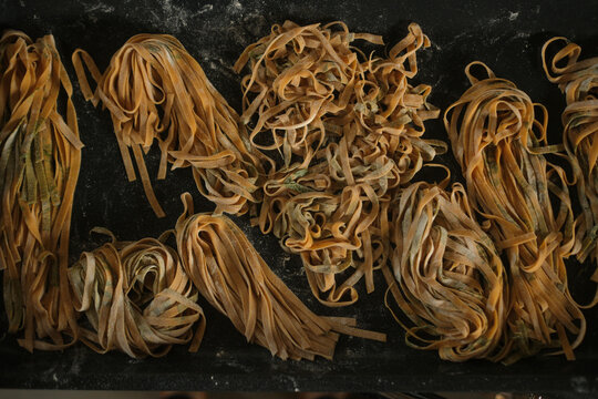 Assorted homemade pasta nests on a dark floured surface, flat lay food photography