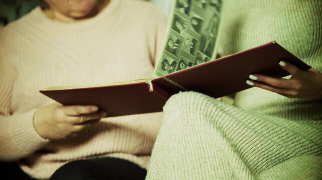 Family Members Looking Through Vintage Photo Album at Home. People Remembering Past Events and Genealogy. Family Tree Documentation
