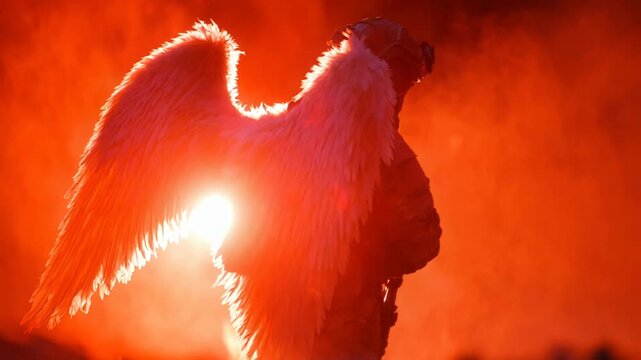 Soldier with angel wings standing in a fiery red haze holding a weapon during sunset