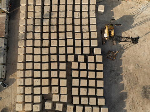 Aerial view of large concrete blocks arranged in a grid pattern next to a yellow construction crane on an industrial site in Priolo Gargallo, Sicily, Italy.