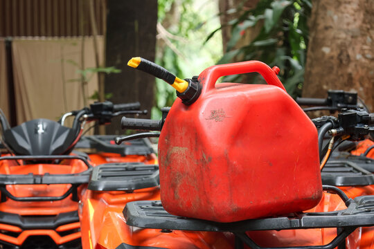 Red plastic fuel can gas container resting on orange offroad atv quad bike vehicle rack outdoors in forest nature park conveying prepared adventurous feeling for extreme recreation trail ride