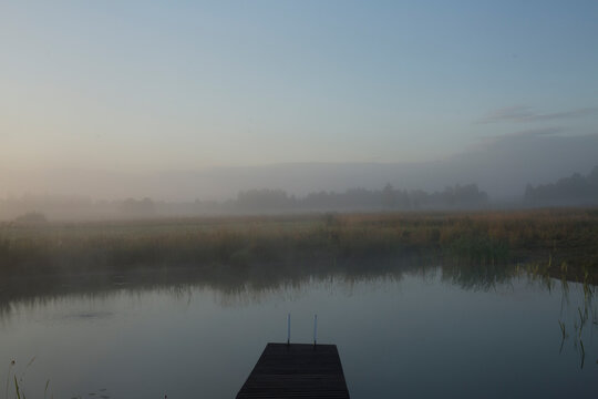 Wooden dock leading into a calm pond on a misty summer morning