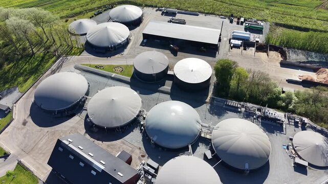 High-angle drone shot capturing the circular storage tanks and infrastructure of a biogas facility near Hammel, Denmark, during a sunny spring day.