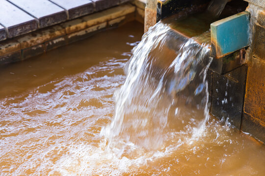 Hot onsen water flowing from a wooden pipe into a bath