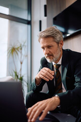 Mature CEO reading email on laptop while working in office.