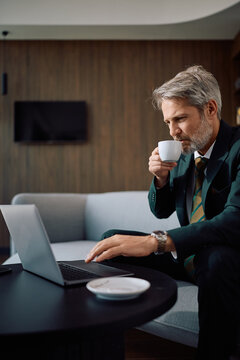 Matures businessman working laptop while drinking coffee in office.