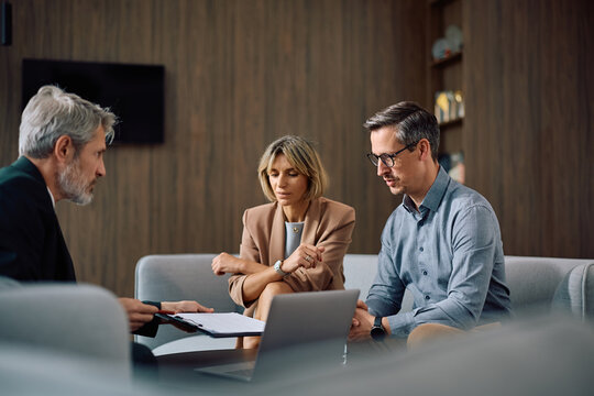 Middle aged couple going through paperwork with financial advisor during meeting in office.