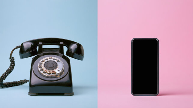 Old black rotary phone sits next to modern black smartphone. Objects on pastel blue and pink backgrounds contrast old versus new communication tech. Evolution from analog to digital devices.