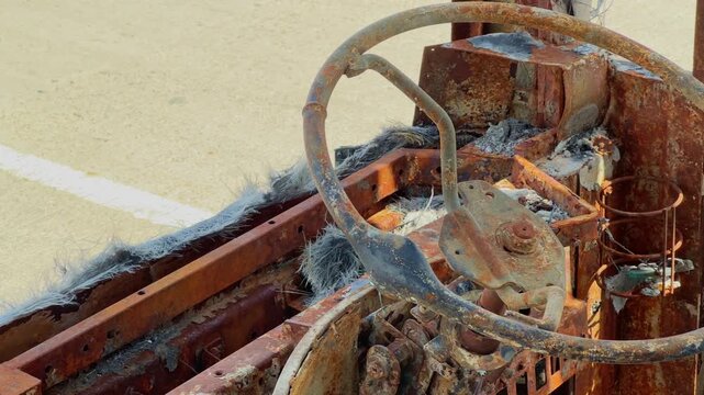 Closeup of rusted steering wheel and destroyed driver cabin inside a fire damaged sleeper bus with charred metal remains and ash!