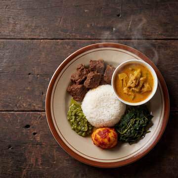 Authentic Indonesian Nasi Padang Plate with White Rice Rendang Beef Gulai Nangka Sambal Hijau Telur Balado and Sayur Daun Singkong on Wooden Table