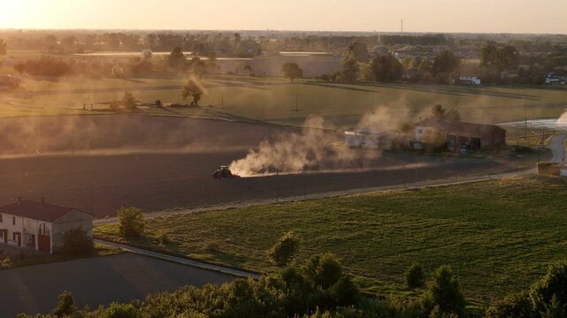 Golden hour sunset over Po Valley farmland with tractor plowing fields