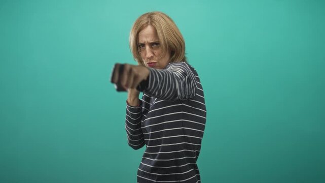 Woman with fists raised punching forward at camera wearing striped shirt against teal studio backdrop; self defense determination.