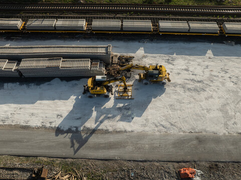Aerial view of yellow excavators working near stacks of concrete railway sleepers on a construction site in Priolo Gargallo, Sicily, Italy.