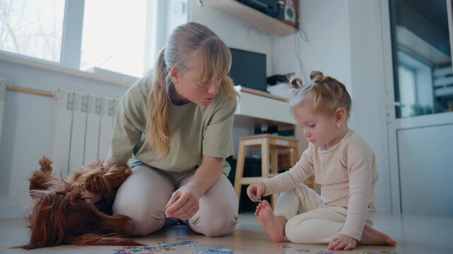 Mother and toddler focus on colorful puzzle on floor. Soft light fills room with calm, cozy feel. Dog rests nearby, adding warmth to scene. Ideal for family bonding, early childhood education