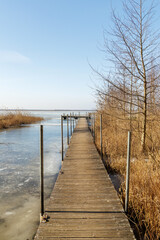 Fototapeta premium Perspective of Wooden Pier Over Frozen Lake in Spring