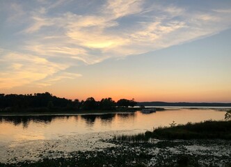 Obraz premium Stunning sunset over a calm river bordered by lush forests and rolling hills. Warm evening light reflects on the tranquil water, creating a peaceful natural landscape ideal for themes of wilderness