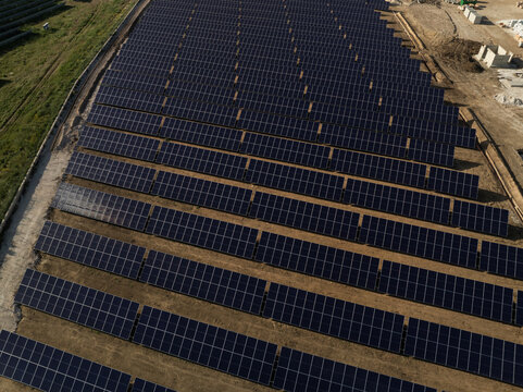 Aerial view of a large solar panel farm with rows of photovoltaic modules installed on open ground in Priolo Gargallo, Sicily, Italy.