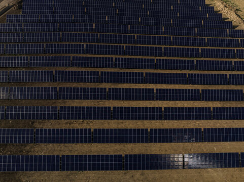 Aerial view of a large solar panel array arranged in neat rows on dry ground in Priolo Gargallo, Sicily, Italy.