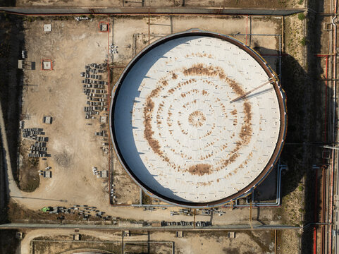 Aerial view of a large industrial storage tank with a white circular roof and concentric rust patterns at an oil refinery in Priolo Gargallo, Sicily, Italy.