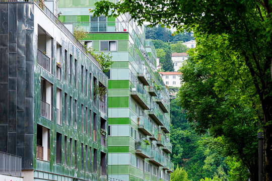 Green balconies run along La Confluence apartments in Lyon, where urban residential architecture and housing extend through a shaded facade in France