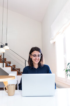 Woman smiling using laptop at home office desk