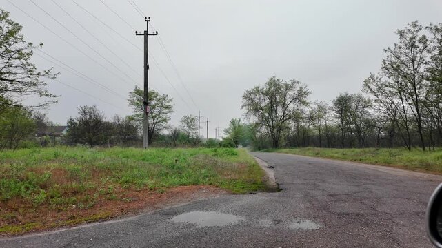 Slow-motion video shot from a moving silver car's perspective on a bumpy asphalt road in the countryside. The car's body 