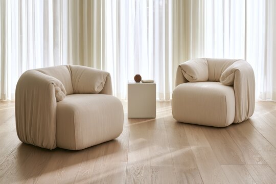 Upholstered cream armchairs arranged in a minimalist sunlit lounge with sheer curtains and wooden floors for interior design branding